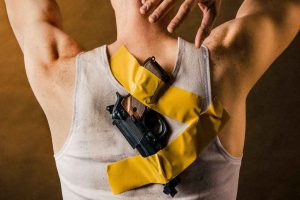 Photograph of a man with a gun taped to his back with yellow tape.