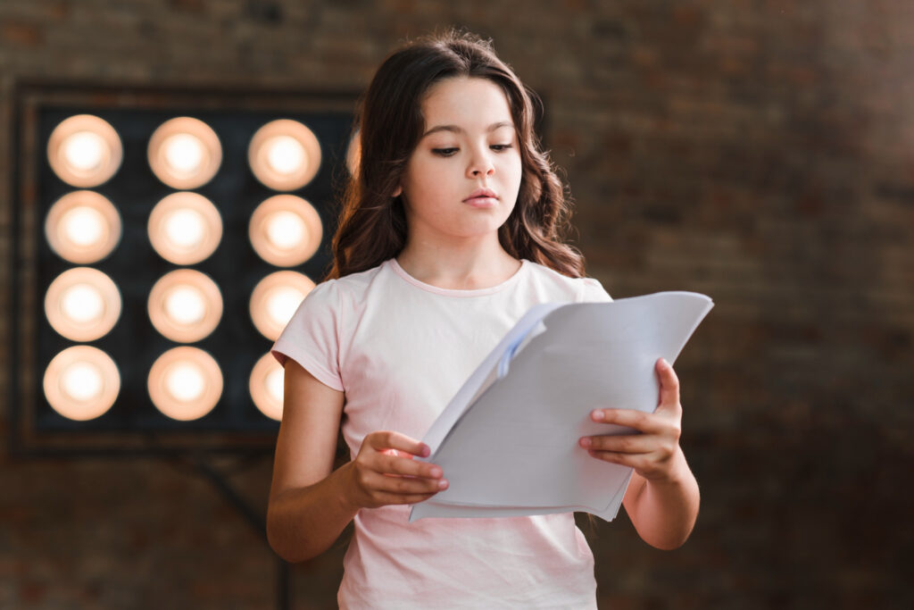 girl reading script standing against stage light