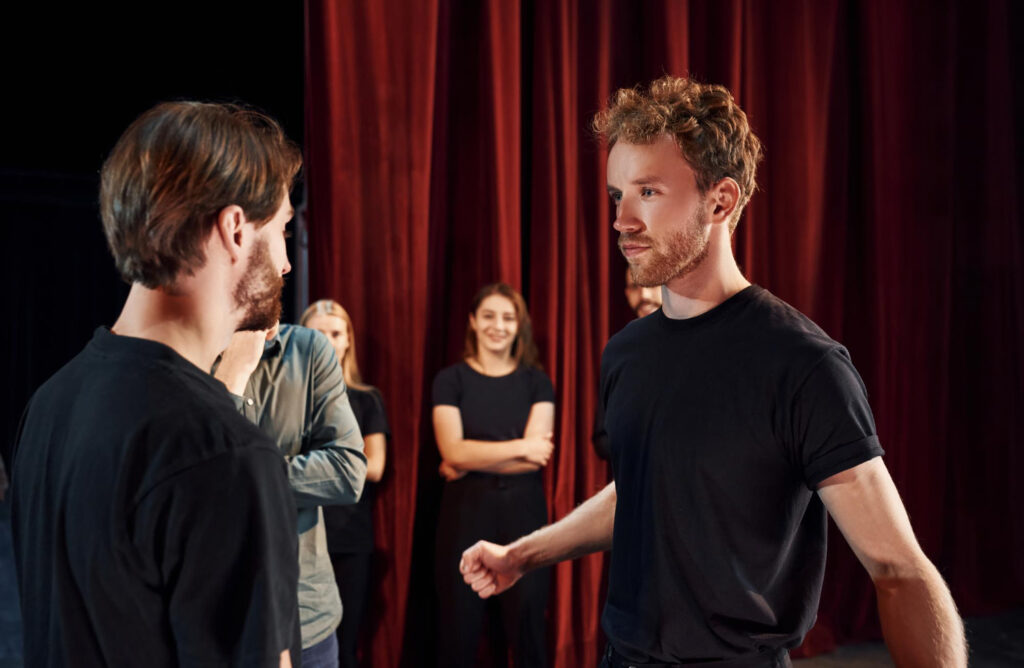 two people talking group actors dark colored clothes rehearsal theater (1)