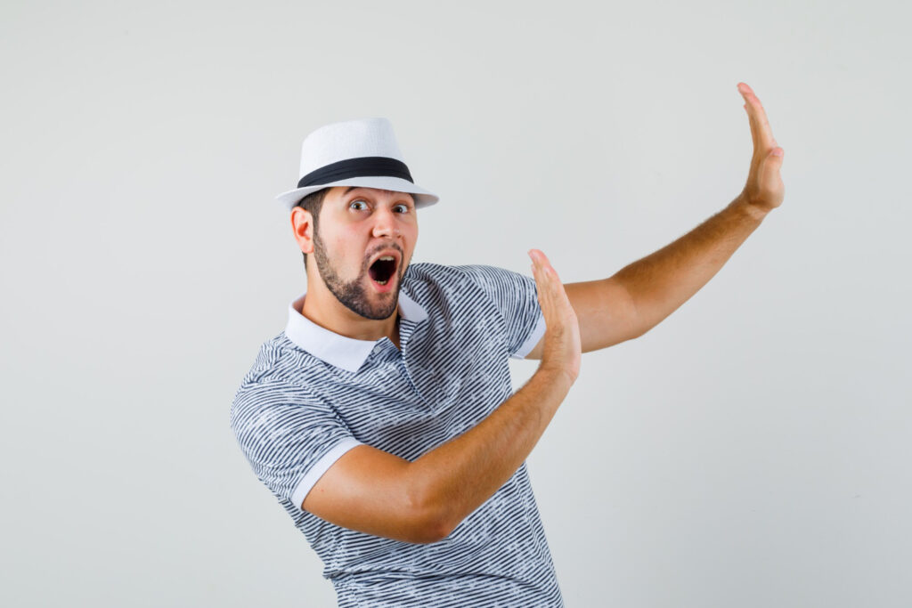 young man raising arms preventive manner hat striped t shirt looking prompt front view