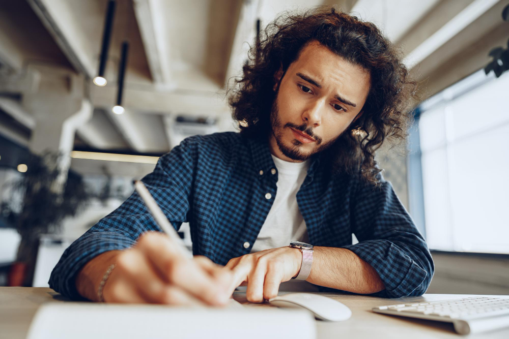 handsome curly guy is making notes working table open space office