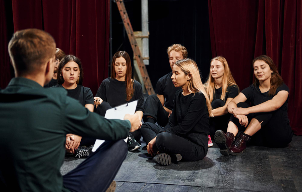 sitting floor group actors dark colored clothes rehearsal theater