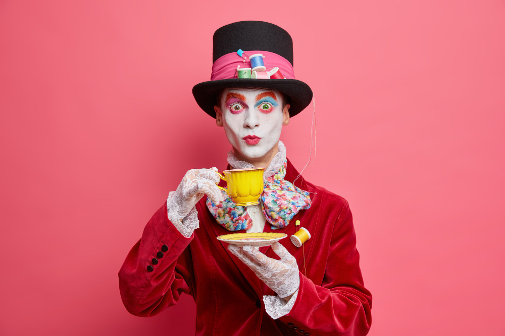 surprised gentleman has image character from wonderland wears aristocratic costume lace gloves hat drinks tea has colorful skull makeup isolated pink wall