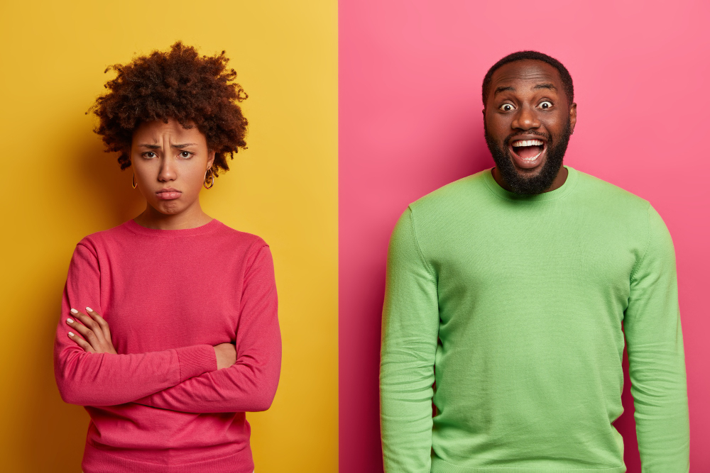 unhappy offended woman stands with arms crossed doesnt speak husband joyful bearded man has dark skin giggles positively something funny expresses positive emotions people reaction